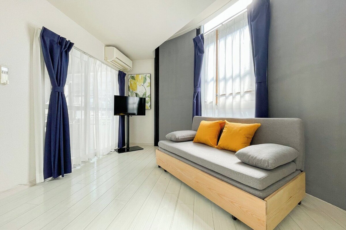 A modern room with a built-in sofa bed, a flat-screen TV, and large windows with curtains.