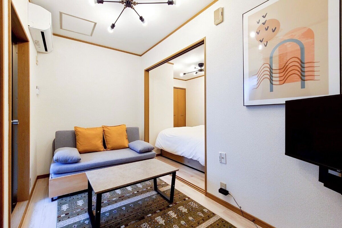 A compact room with a sofa, a bed, a TV, and a ceiling fan.