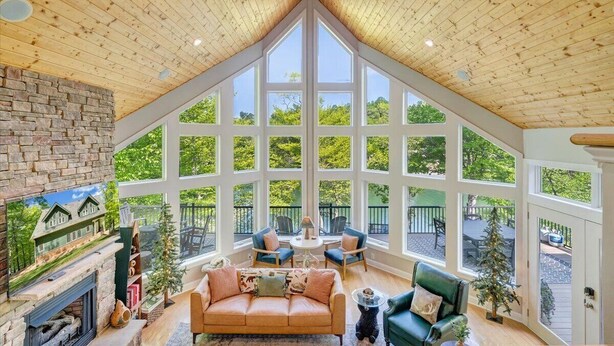 A cozy interior with a fireplace, a green sofa, and a dining area with chairs. - The Lakeside Lodge - 6BR Luxury Lakefront Property - Private Dock (Moneta)