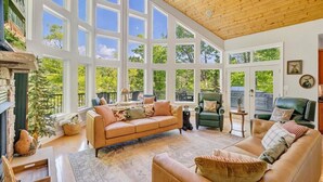 A spacious living room with a large window, a fireplace, and a green leather sofa. - The Lakeside Lodge - 6BR Luxury Lakefront Property - Private Dock (Moneta)