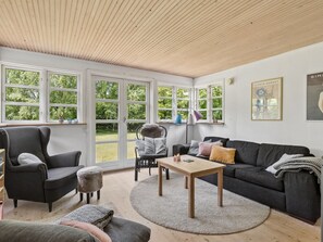 A modern living room with a wooden ceiling, large windows, a grey sofa, a wooden coffee table, and a chair with a fluffy cushion. - "Niela" - 400m from the sea by Interhome (Kalundborg)