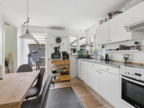 Ett modernt kök med vita skåp, ett matbord i trä, en inbyggd ugn och en klocka på väggen.