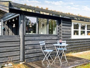 Eine Holzhütte mit einer Terrasse, zwei Stühlen und einem Tisch.