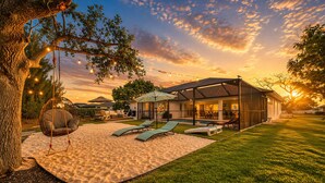 A modern house with a covered patio, a swing chair, and a pool. - Luxury Canal Villa, Headed Pool, Game Room, Sandy Beach Yard & Fire Pit (Cape Coral)