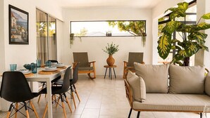 A modern living room with a dining area, a ceiling fan, and large windows. - Luxury Canal Villa, Headed Pool, Game Room, Sandy Beach Yard & Fire Pit (Cape Coral)