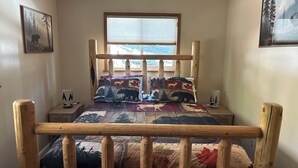 Un lit avec un cadre en bois, une fenêtre avec des stores, une table de chevet avec une lampe et un tableau accroché au mur.