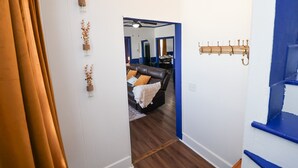 Un couloir avec un rideau marron, un porte-manteau et un salon doté d’un canapé en cuir noir et d’un miroir.