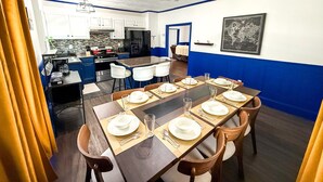 Un espace repas avec une longue table dressée pour six personnes, une cuisine en arrière-plan et une décoration aux couleurs bleu et blanc.