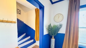 Un escalier aux murs bleus, une horloge accrochée au mur et une plante dans un vase.