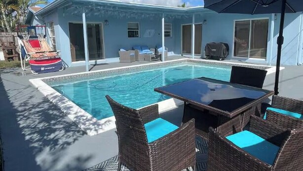 Una piscina con mesa y sillas, una sombrilla y un edificio con puertas de vidrio correderas.