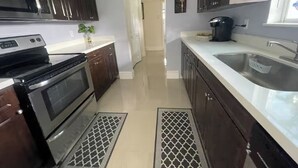 Una cocina con armarios de madera oscura, electrodomésticos de acero inoxidable, una encimera blanca y un fregadero.