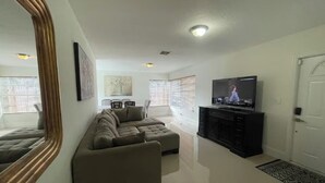 Una sala de estar con sofá, televisión, mueble y puerta.