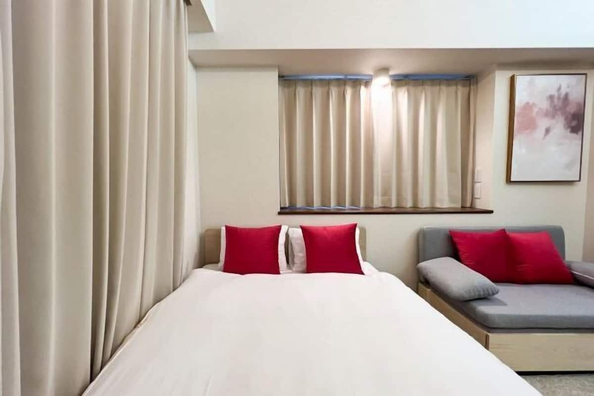 A hotel room with a bed, a sofa, and a window with curtains.