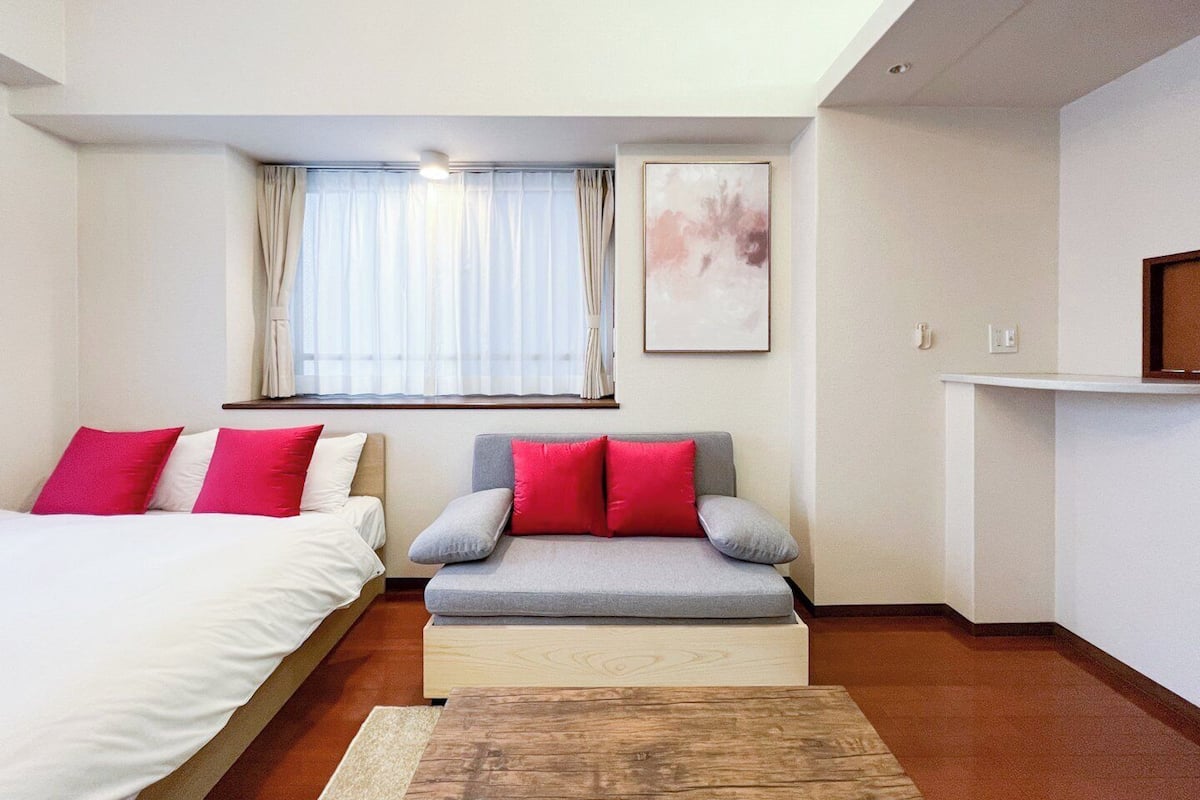 A hotel room with a bed, a sofa, a wooden coffee table, a window with curtains, and a wall-mounted picture.