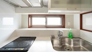 A compact kitchen with a built-in stove, a stainless steel sink, and a window above the sink. - CITYSPIRE Sakurakawa II (Osaka)