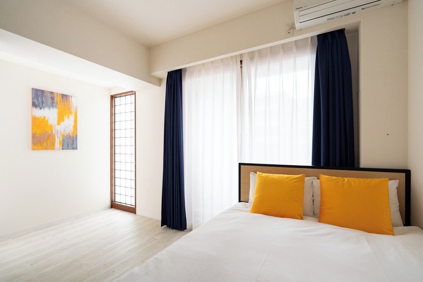 Una habitación de hotel con cama, cortinas, una ventana y un equipo de aire acondicionado.