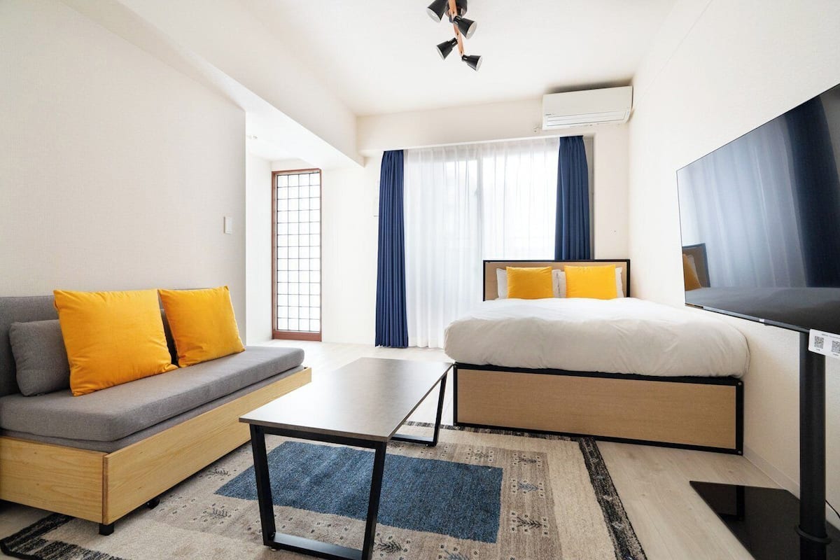 A modern hotel room with a sofa, a bed, a TV, and a window with curtains.
