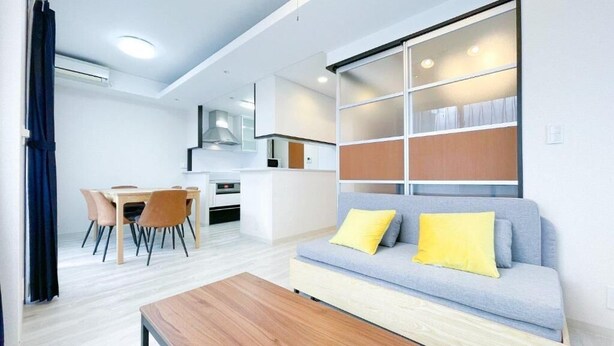 A modern living room with a sofa, coffee table, and dining area. - CITYSPIRE Sakurakawa II (Osaka)