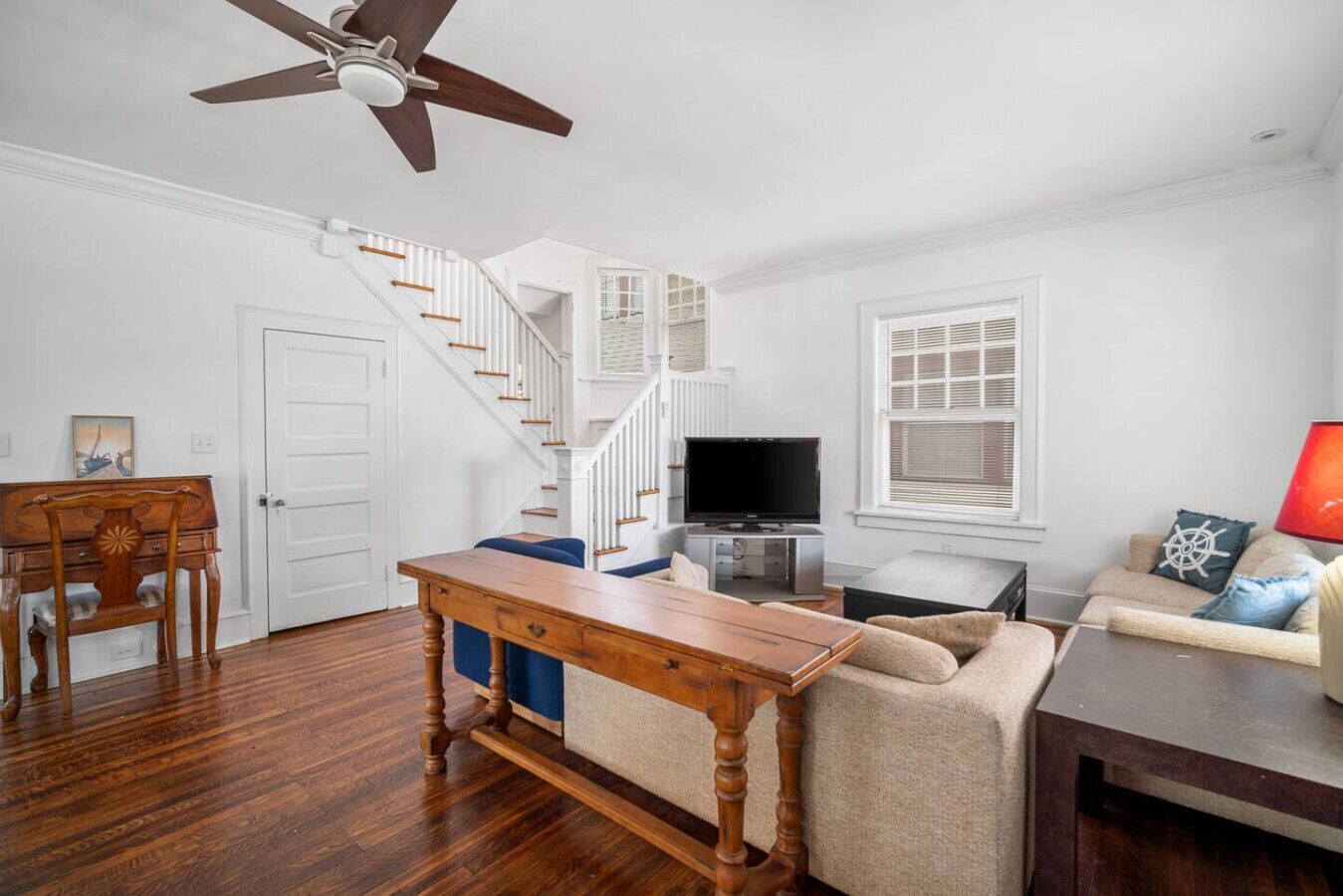 A spacious living room with hardwood floors, a wooden dining table, a sofa, a TV, and a ceiling fan.
