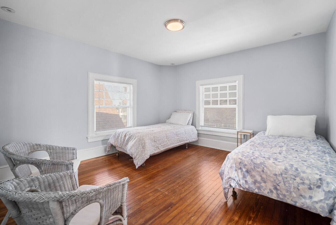 A bedroom with two beds, a chair, and a window.
