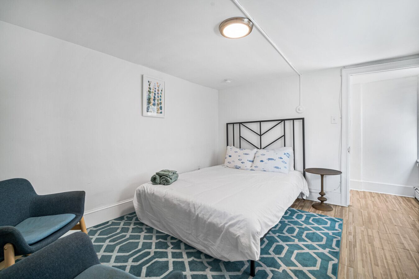 Une chambre à coucher comprenant un lit, une chaise, une petite table, un tapis à motifs et une œuvre d’art murale.