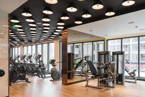 Un gimnasio con máquinas de cardio, estaciones de pesas y espejos.