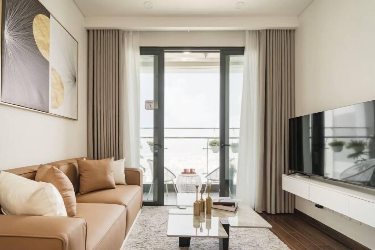 A modern living room with a sofa, a coffee table, a flat-screen TV, and a balcony with a view.