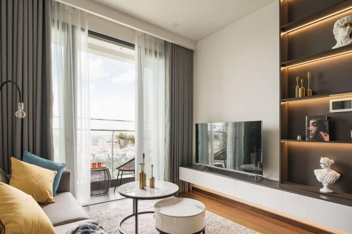 A modern living room with a sofa, a round coffee table, a TV, and a bookshelf with decorative items.
