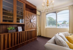 A room with a wooden cabinet, a sun-shaped wall decoration, a chandelier, and a view through a window. - Retro 3BR Mid Century Apartment (St Kilda East)