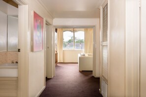 A hallway with a bathroom on the left, a window with curtains, and a white sofa in the distance. - Retro 3BR Mid Century Apartment (St Kilda East)