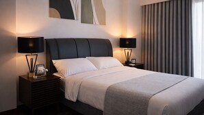 Quarto de hotel moderno com uma cama grande, duas mesas de cabeceira e arte abstrata na parede.