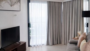 Uma sala de estar moderna com televisão de tela plana, sofá, mesa de centro e uma grande janela com cortinas.