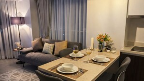 Uma área de refeições moderna com uma mesa posta para dois, um sofá e uma cozinha ao fundo.