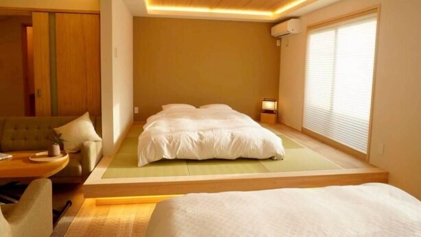A modern hotel room with a bed, a sofa, a small table, and a window with blinds. - koyado Nagomi (Kobe)