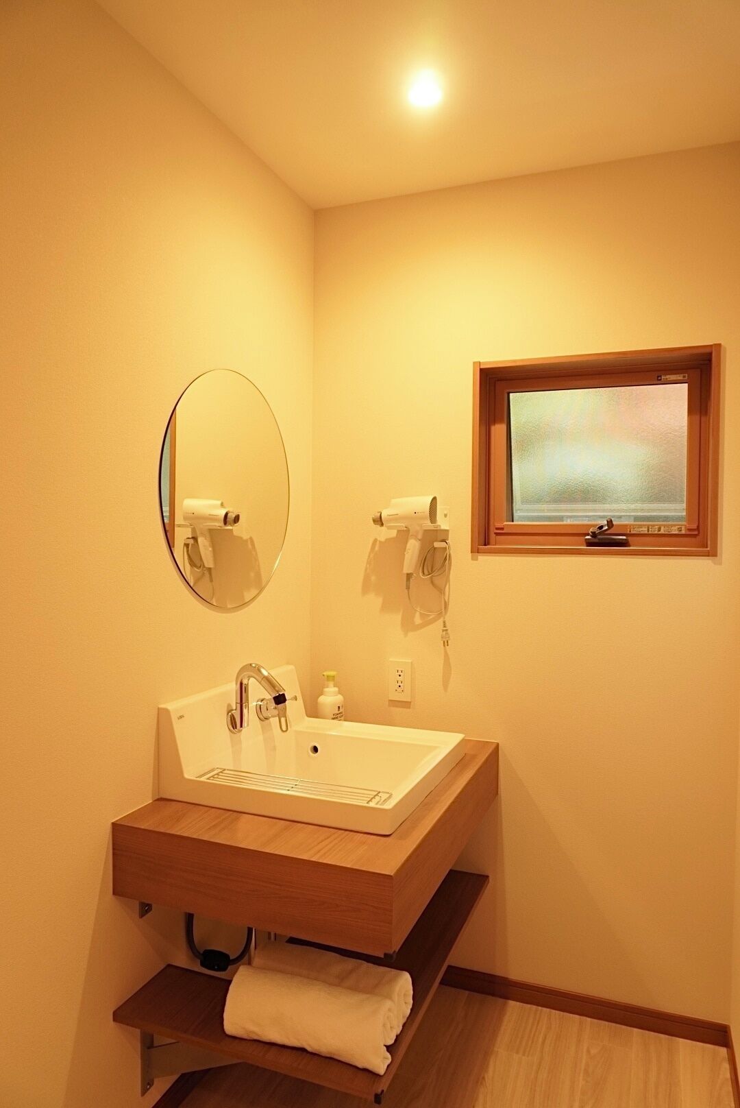 Un baño con lavamanos, espejo, toallero, ventana y un estante pequeño.
