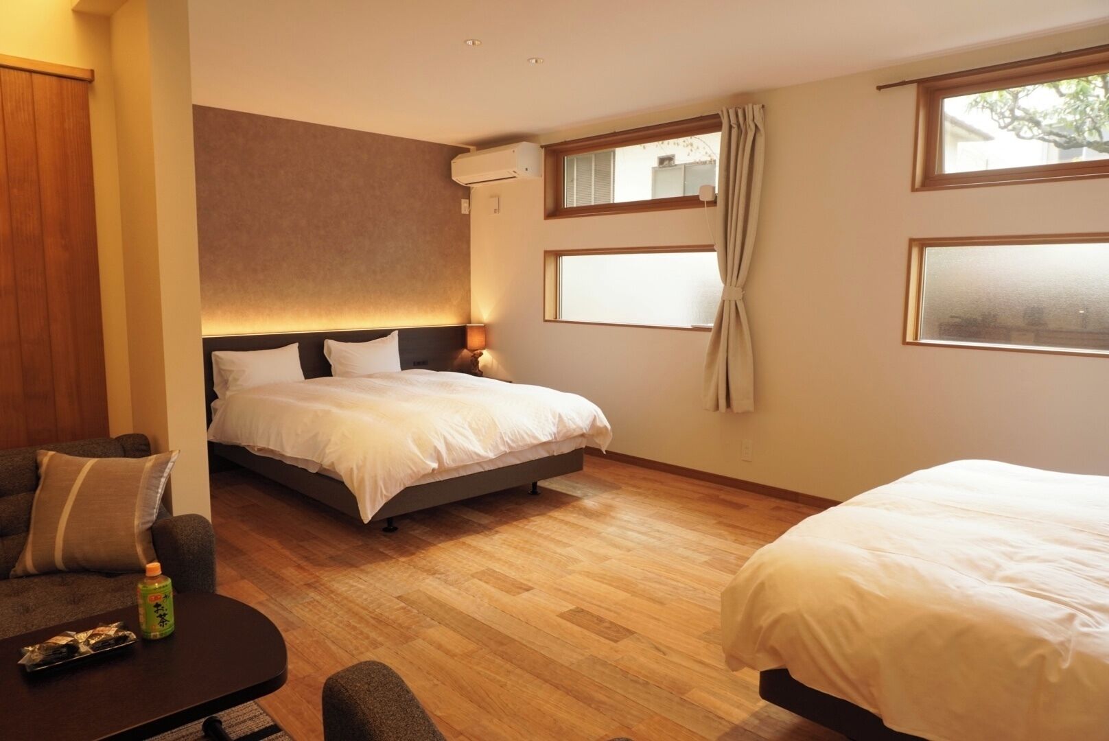 A hotel room with a bed, a sofa, a small table with a bottle, and a window.