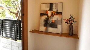 A room with a wooden shelf, a painting, and a vase with flowers. - koyado Nagomi (Kobe)