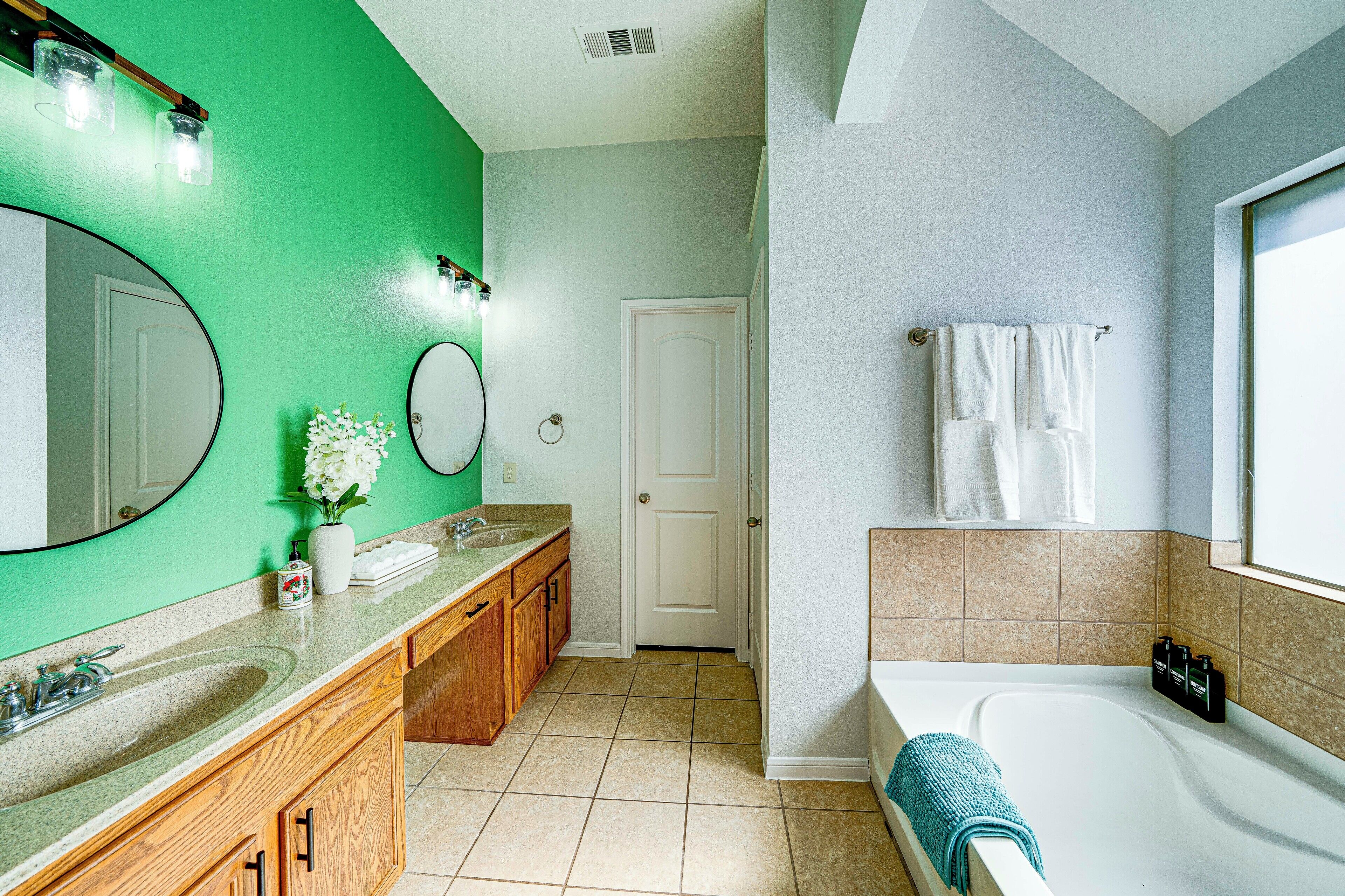 A bathroom with a green wall, a white door, a bathtub, and a vanity with a mirror.