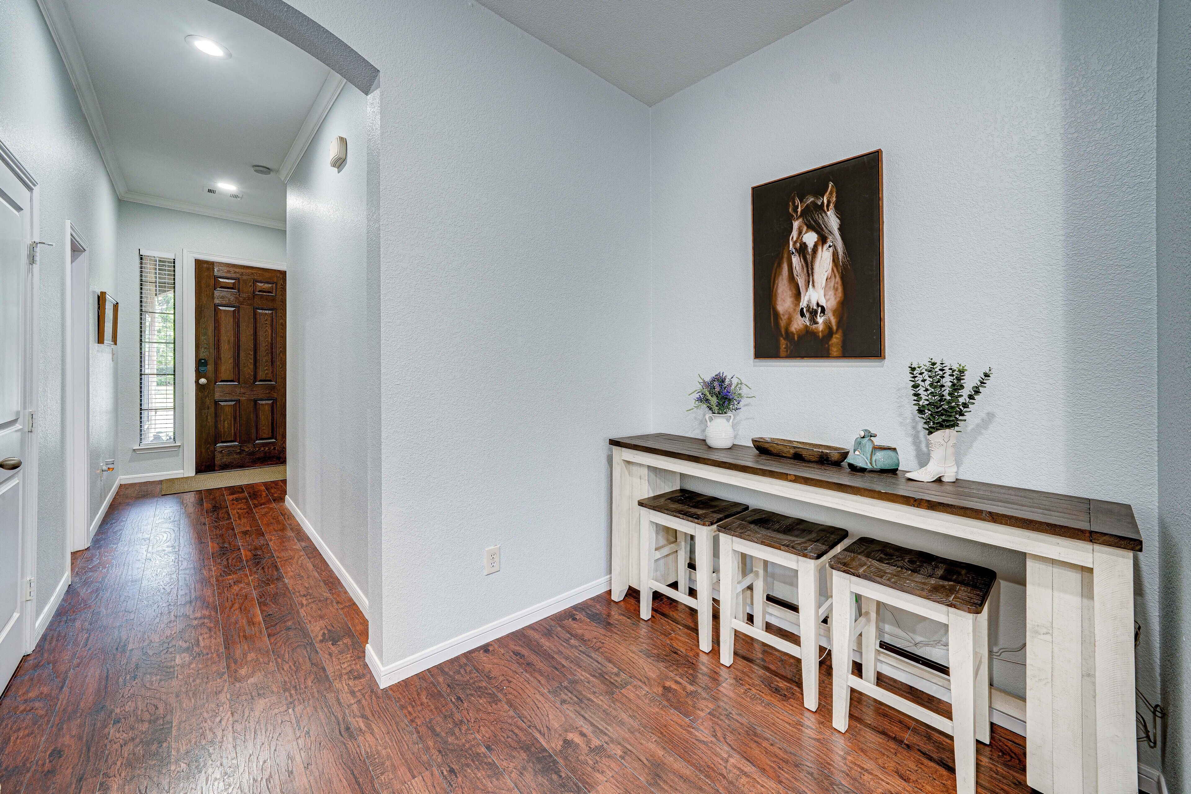 Un pasillo con suelo de madera, pared blanca, puerta de madera y un banco con taburetes.