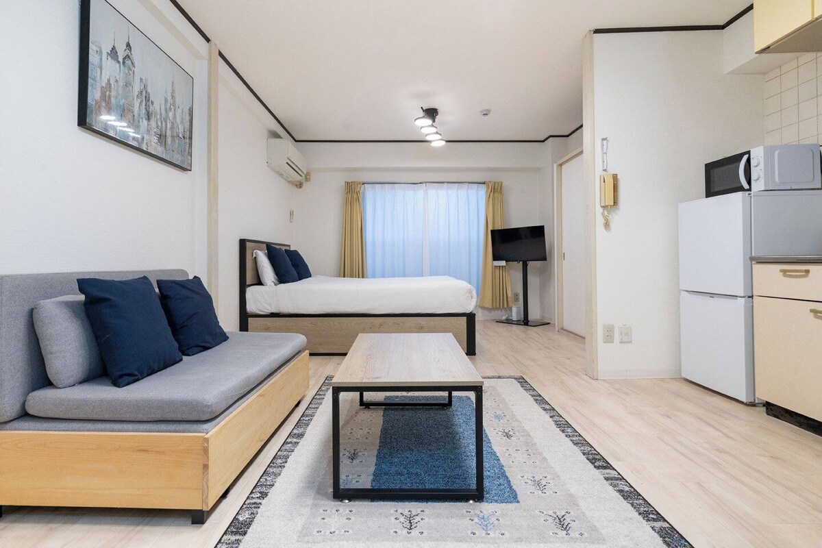 A modern hotel room with a sofa, bed, TV, and kitchenette.