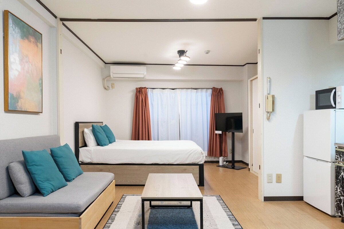 A hotel room with a bed, a sofa, a TV, a microwave, and an air conditioning unit.