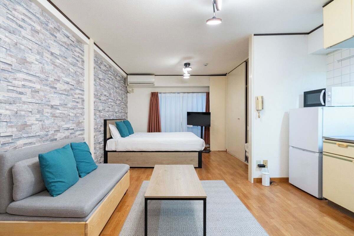 A compact hotel room with a bed, sofa, kitchenette, and a stone wall.