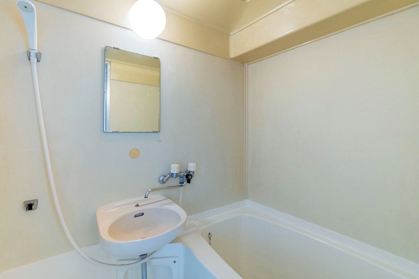 A bathroom with a white sink, a mirror, a bathtub, and a showerhead.