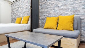 Una habitación con un sofá gris, dos almohadones amarillos, una mesita gris y una pared con diseño de piedra.