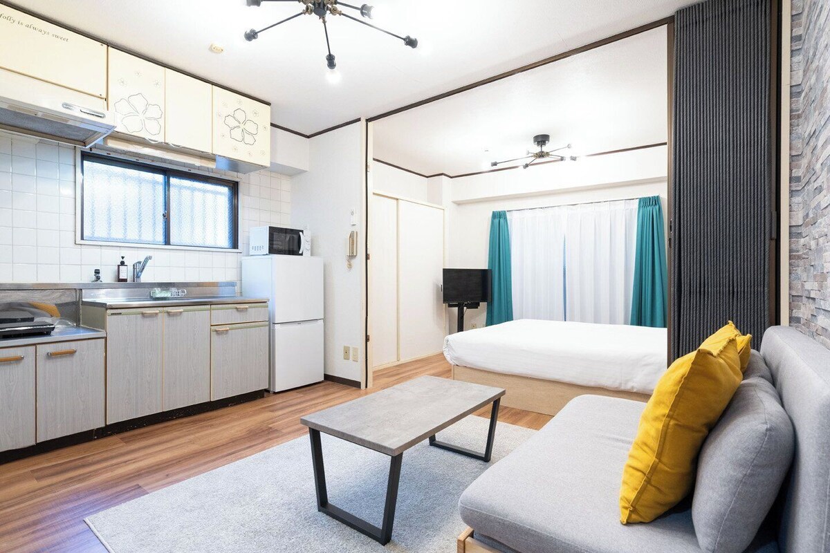 A compact hotel room with a kitchenette, a bed, a sofa, and a small table.