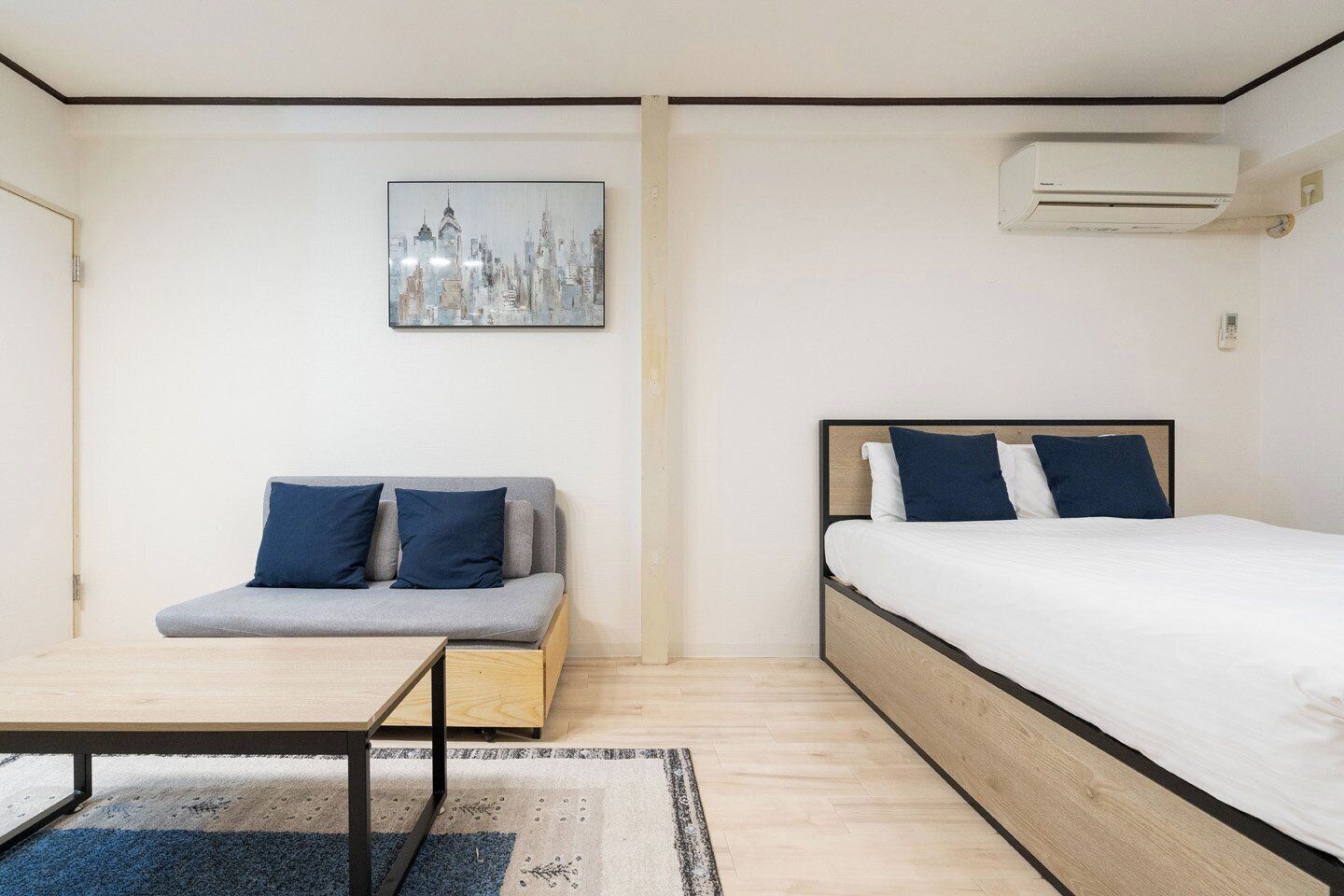 A bedroom with a bed, a sofa, a small table, and an air conditioning unit.