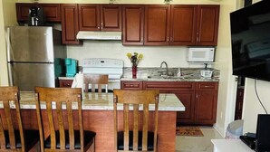 Una cocina con armarios de madera, un refrigerador de acero inoxidable, un microondas y un televisor.