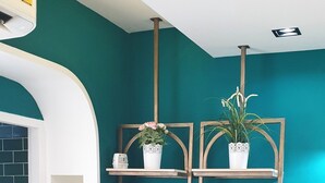 A teal-colored wall with a white shelf unit, a hanging rack, and a small table. - Family Hub at Pratunum (Bangkok)