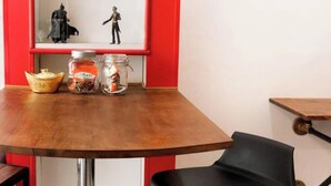 A room with a wooden table, a black chair, a shelf with figurines, and jars with spices. - Family Hub at Pratunum (Bangkok)