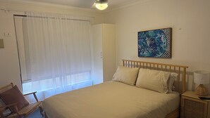 A bedroom with a bed, a chair, a nightstand, a lamp, a ceiling fan, and a window with curtains. - Villa Quindy - ideally located a short 2 minute stroll to Quindalup bay beach. (Quindalup)